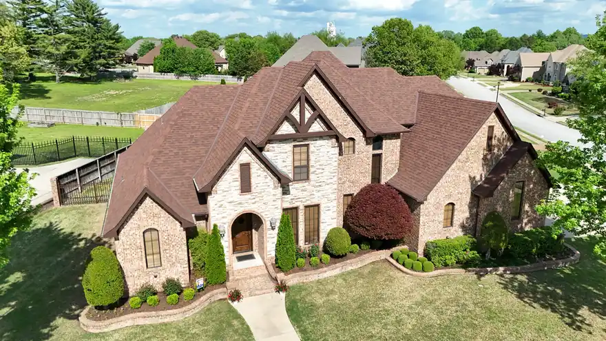 Tudor stone and brick home with a new terracotta-tone shingle roof, seen from above