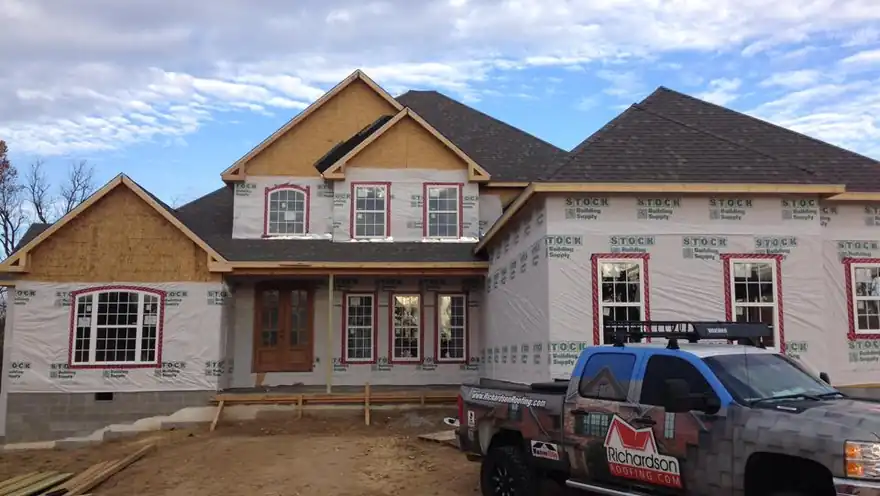 New-build home wrapped in house wrap beside a Richardson Roofing branded camo pickup